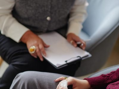 Woman holding tissue sitting across from woman with clipboard conducting counseling session in office setting
