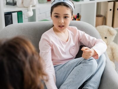 Preteen child talking to blurred psychologist in consulting room